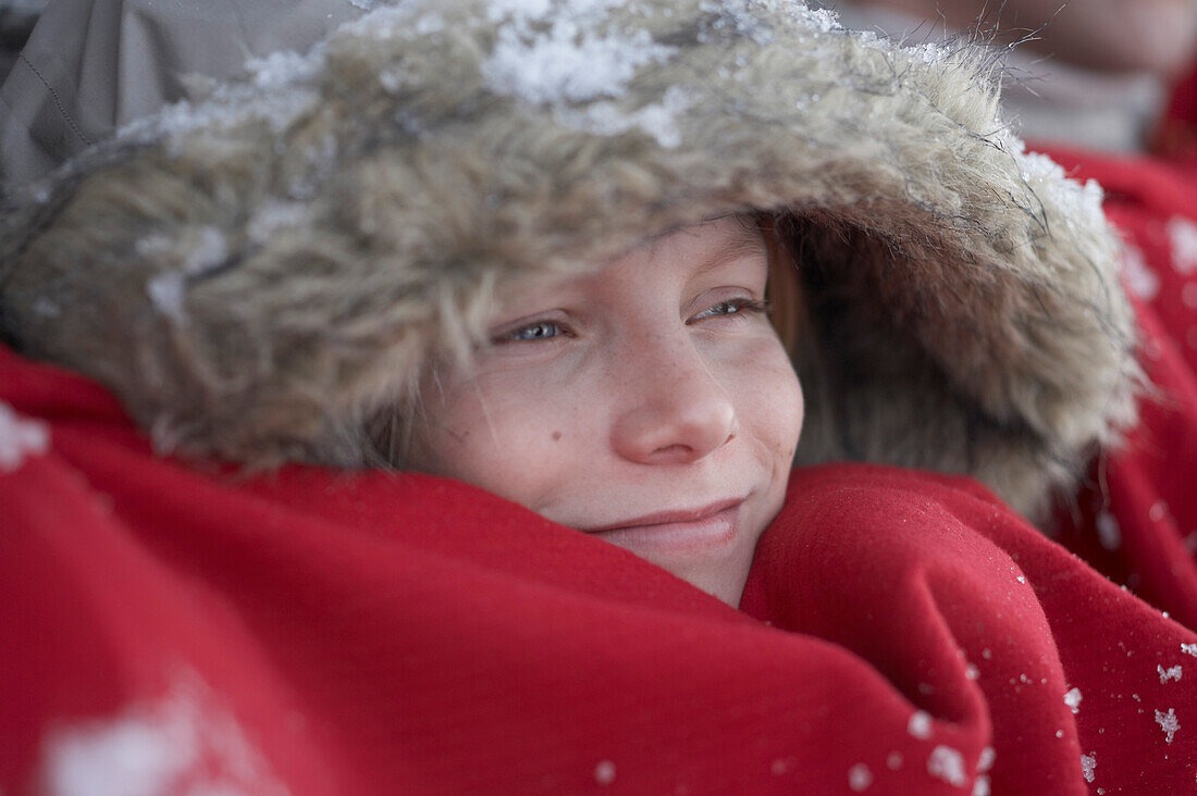 Parents and son leaning on wooden hut, warming with red blanket