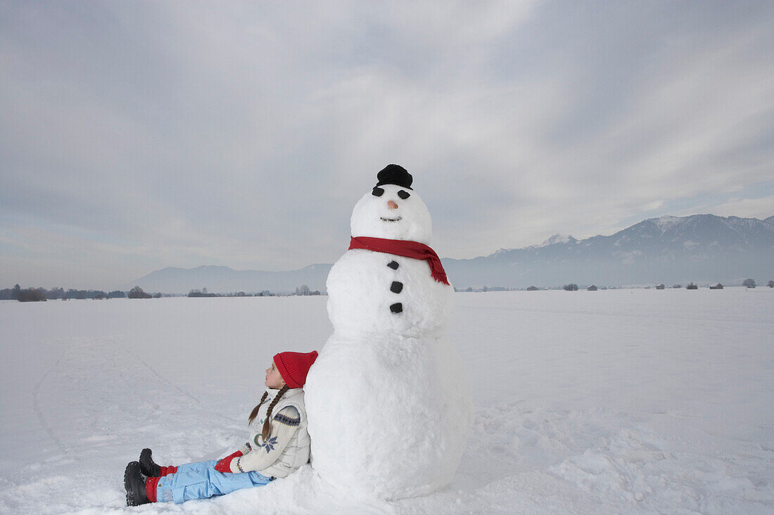 Mädchen 5-6 Jahre, lehnt an einem Schneemann