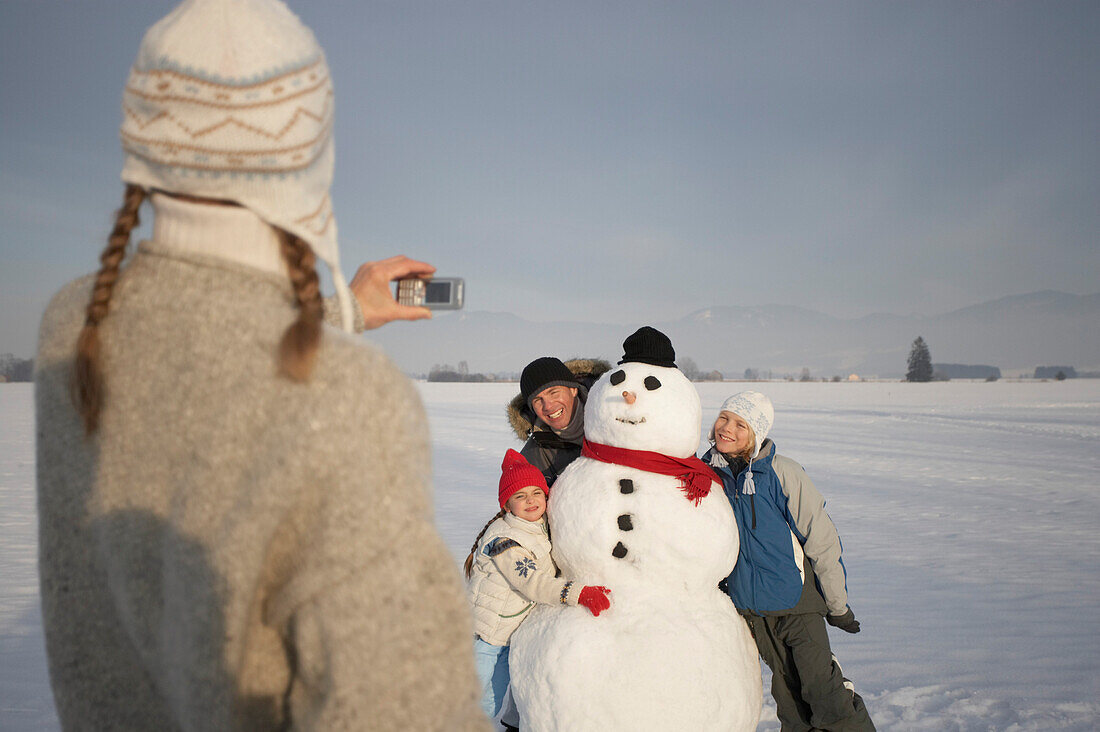 Familie und Schneemann werden von der Mutter fotografiert