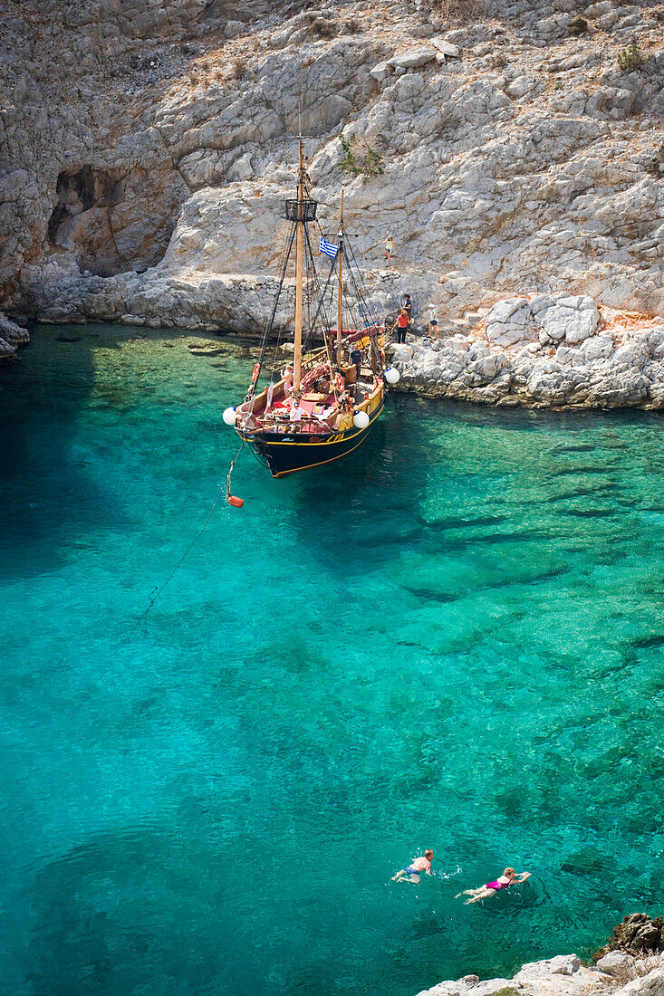People swimming in a bay of Kalymnos next to a sailing boat, Greece