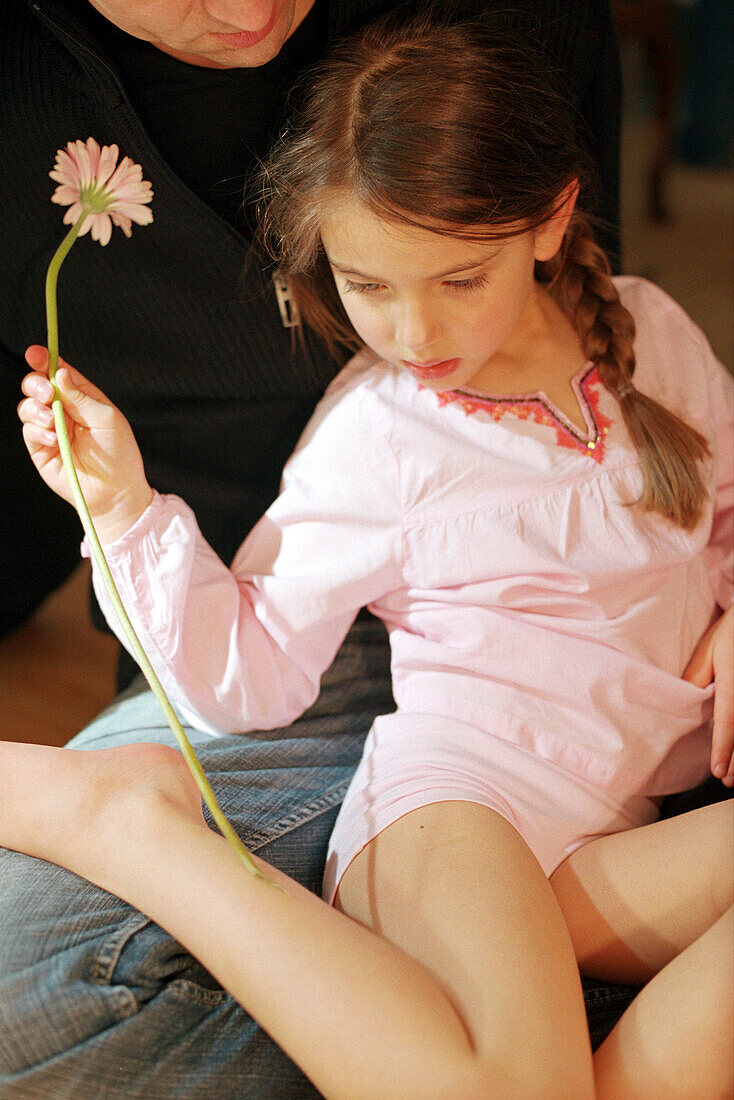 Girl sitting on fathers lap, holding flower in her hand