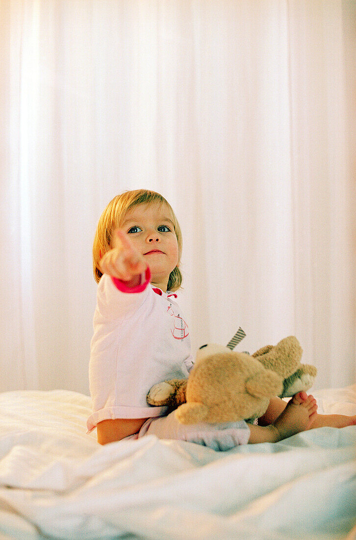 Toddler girl sitting with teddy on bed, Portrait
