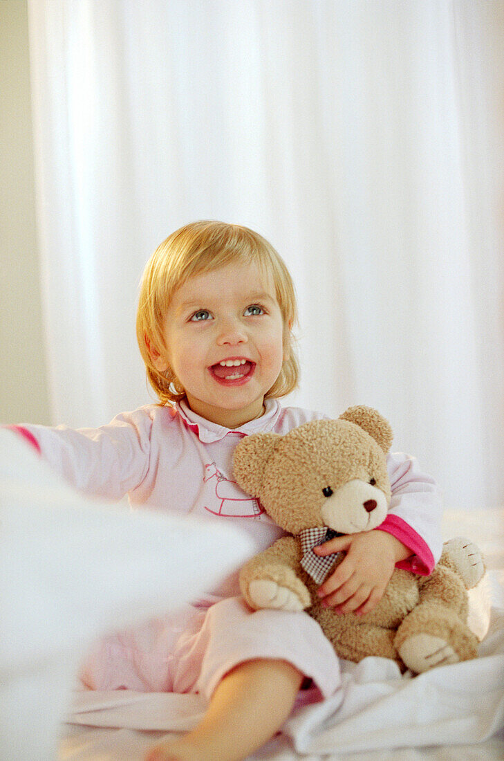Toddler girl holding her teddy in bedroom