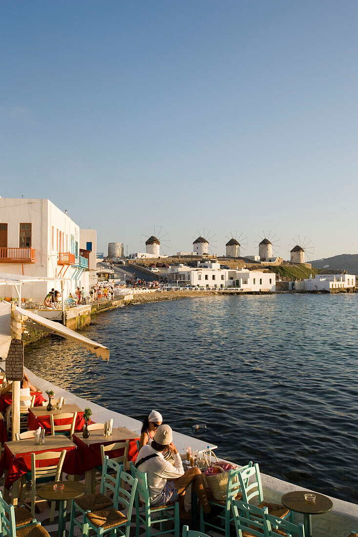 People sitting in restaurants and bars directly at sea, windmills in background, Little Venice, Mykonos-Town, Mykonos, Greece