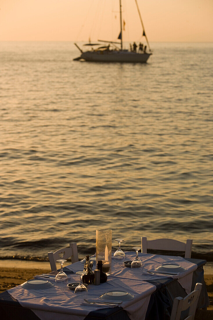 View over a table with glasses and plates to a sailingboat on the sea, Little Venice, Mykonos-Town, Mykonos, Greece