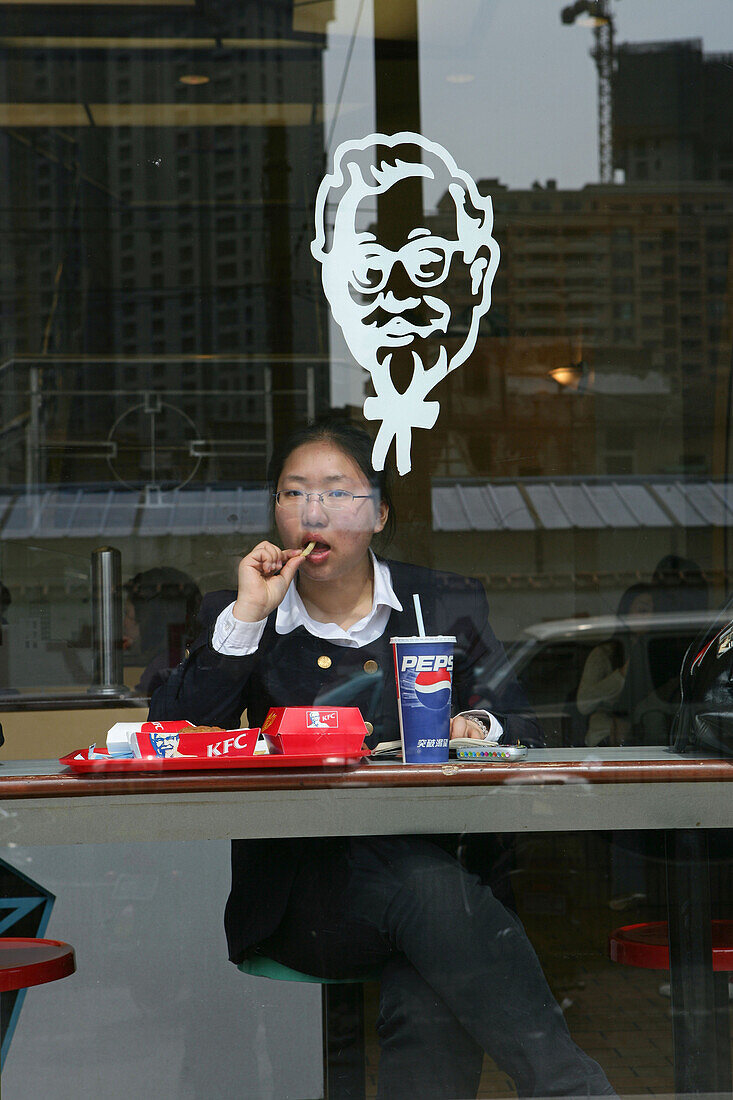 Fastfood restaurant window, woman eating American fastfood, KFC, Pepsi