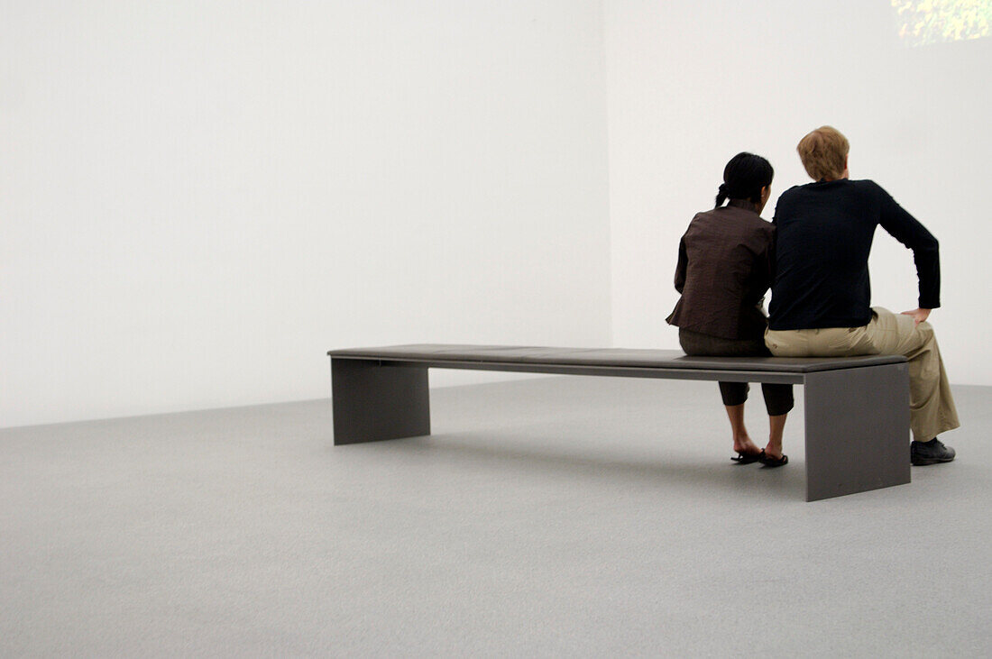 Couple sitting on bench in museum, Pinakothek der Moderne Munich, Bavaria, Germany