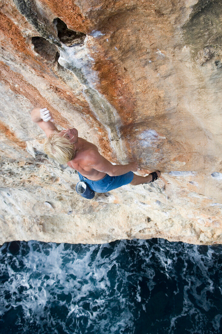 Man climbing on rock face over water, Coast of Majorca, Spain
