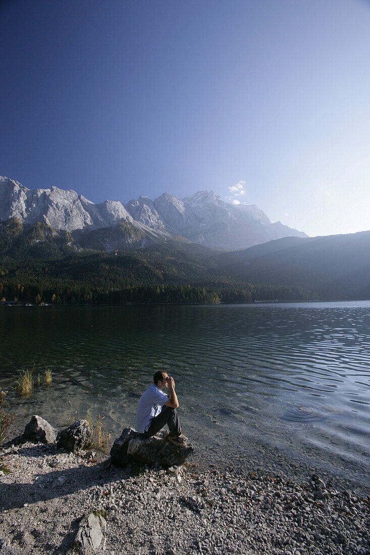 Mann sitzt am Eibsee, Zugspitze im Hintergrund, Bayern, Germany