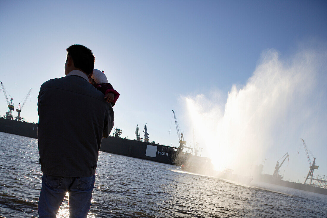 Father holding baby, looking from quay, river Elbe, harbor and docks, St. Pauli, Hamburg, Germany