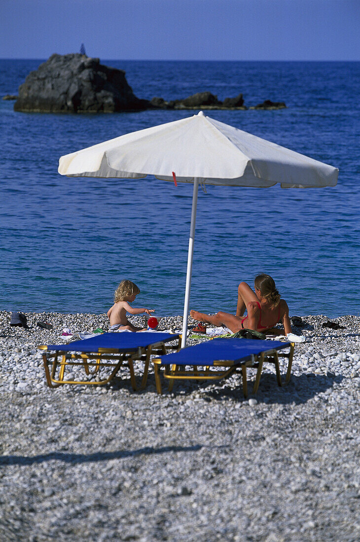 Mother and little child sitting on beach, Karpathos, Dodecanese Islands, Greece
