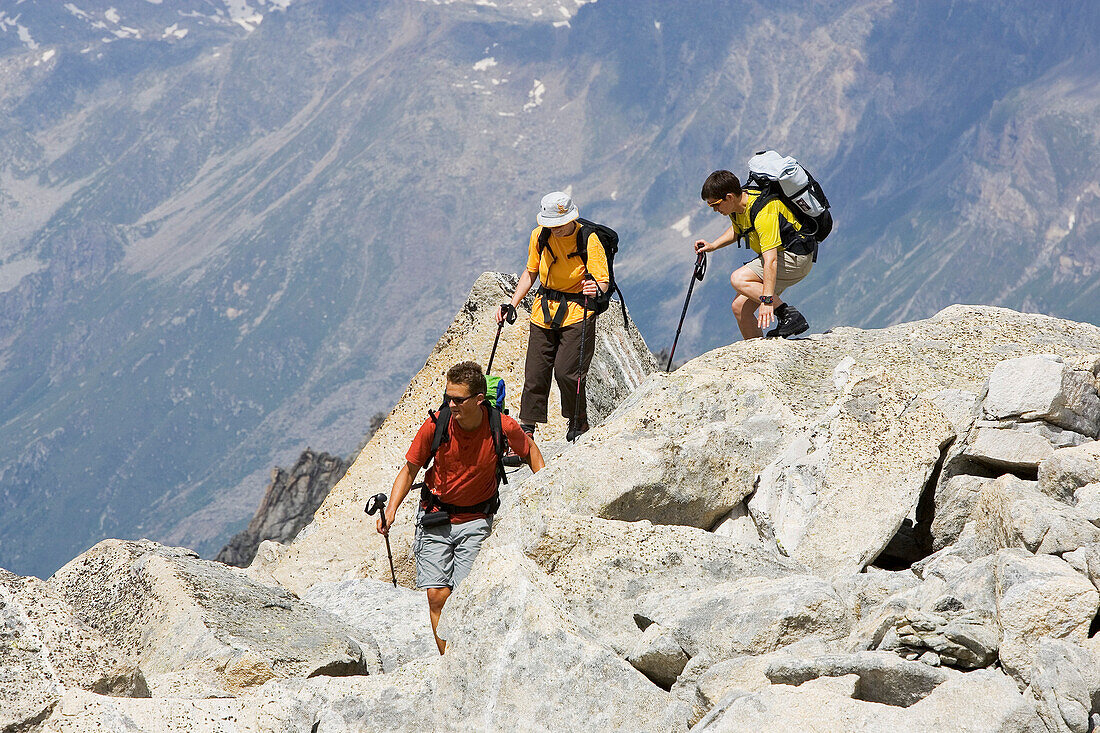 Three people scrambling down a rocky path. Pass da Casnil, Albigna, Bregaglia, Bergell, Graubuenden, Grisons, Switzerland, Alps.