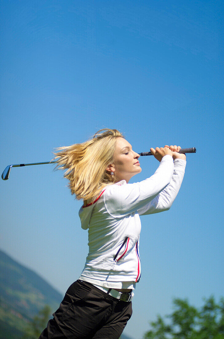 Junge Frau mit blonden Haaren beim Golfen am Abschlag
