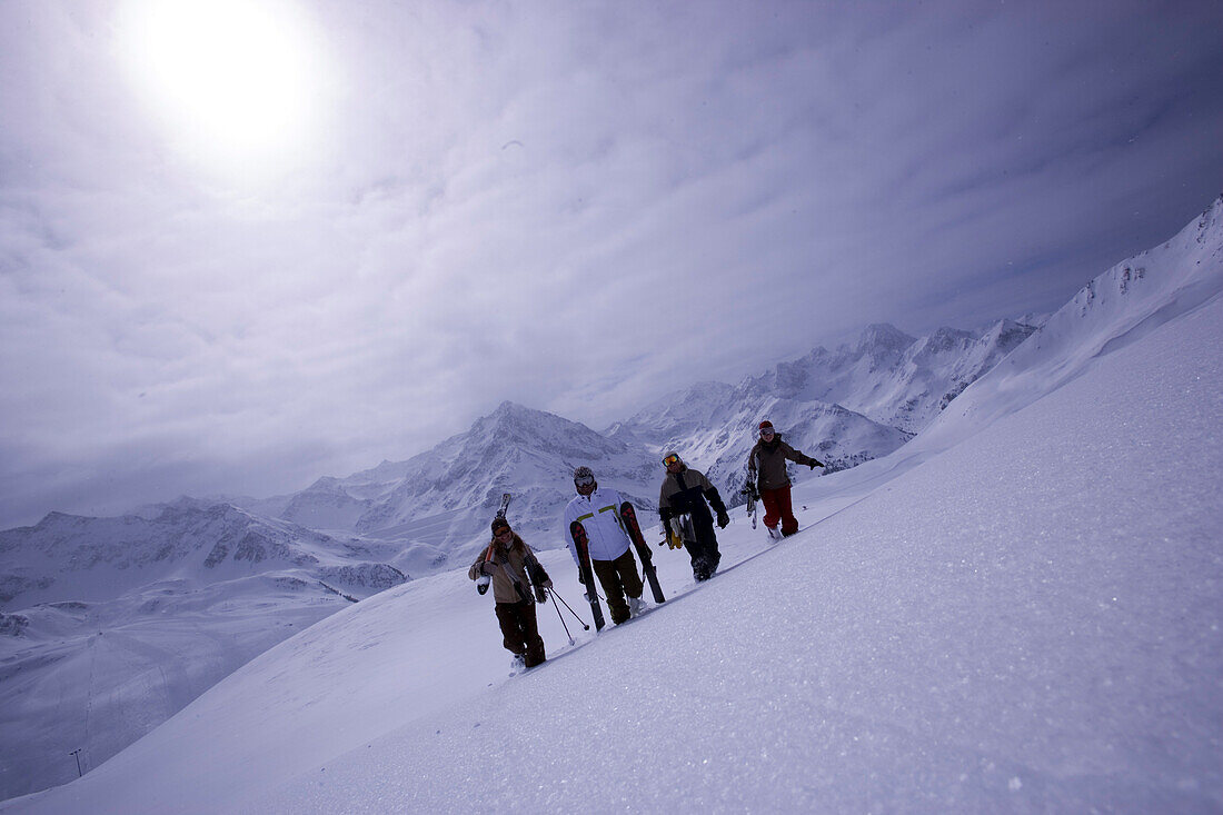 Four people with skies and snowboard walking up a snowcapped mountain, Kuehtai, Tyrol, Austria