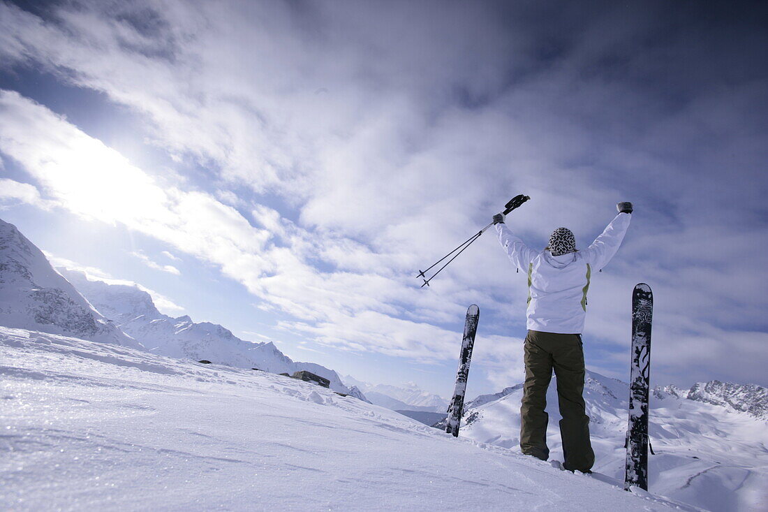 Young man with skis standing on snowcovered mountain, arms rising high, Kuehtai, Tyrol, Austria