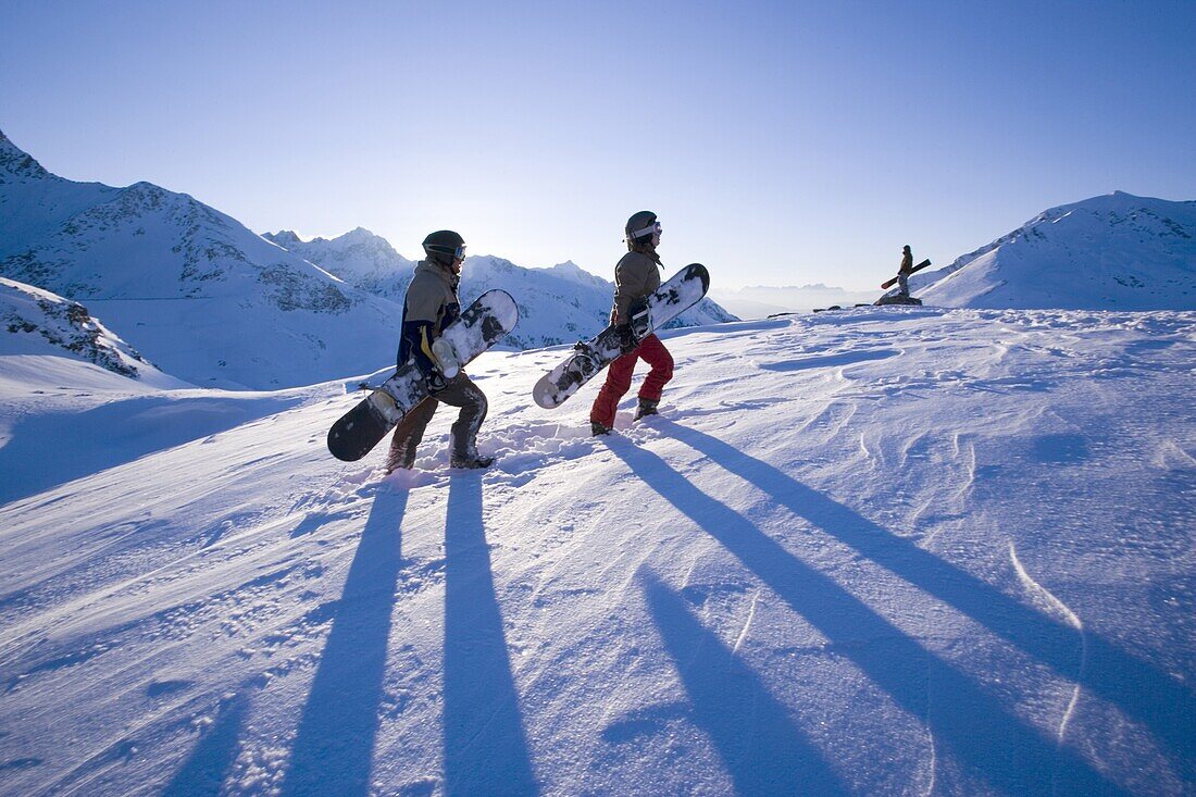 Zwei Personen tragen Snowboards, eine Person steht im Hintergrund, Kühtai, Tirol, Österreich