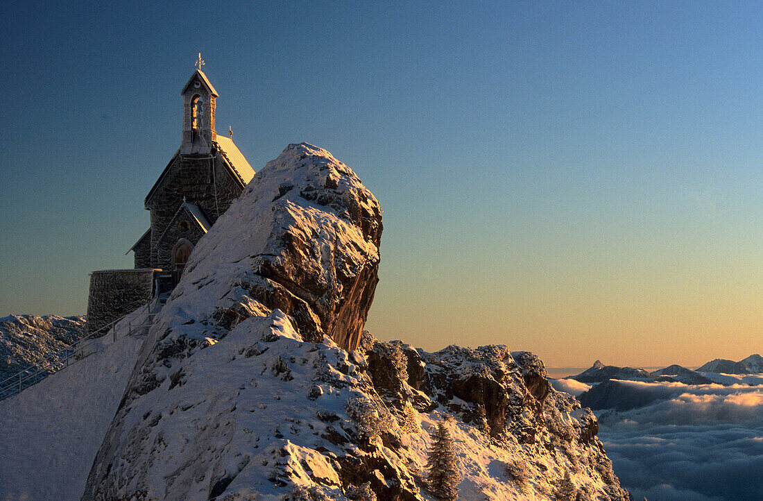 Snow covered chapel on rock formation at dawn, Wendelstein, Bavarian range, Upper Bavaria, Germany