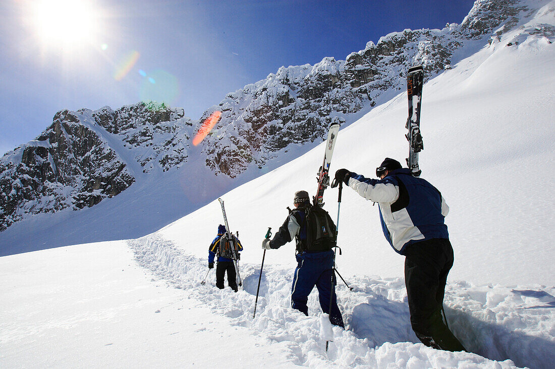 Auf der Suche nach unverspurtem Pulverschnee. Drei Männer tragen ihre Skis zum nächsten Schneehang. Lech, Zürs, Arlberg, Österreich, Alpen, Europa.