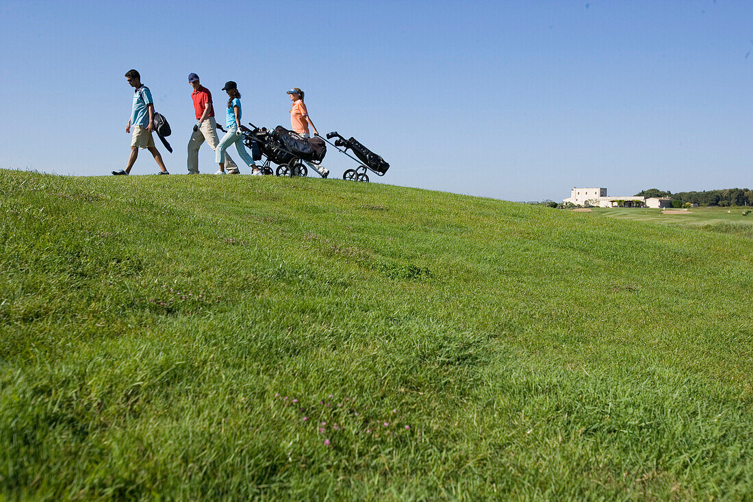 Group of people walking on golf course pulling golf bag on wheels, sideview, Apulia, Italy