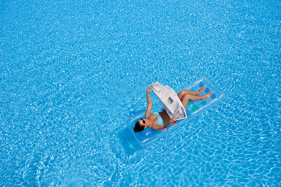 Frau liegt auf Luftmatratze im Pool und liest Zeitung, Apulien, Italien