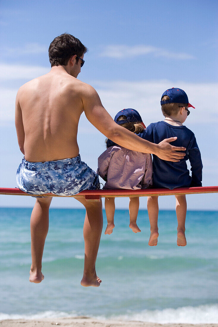 Young man and two children sitting on bench before sea shore, Apulia, Italy