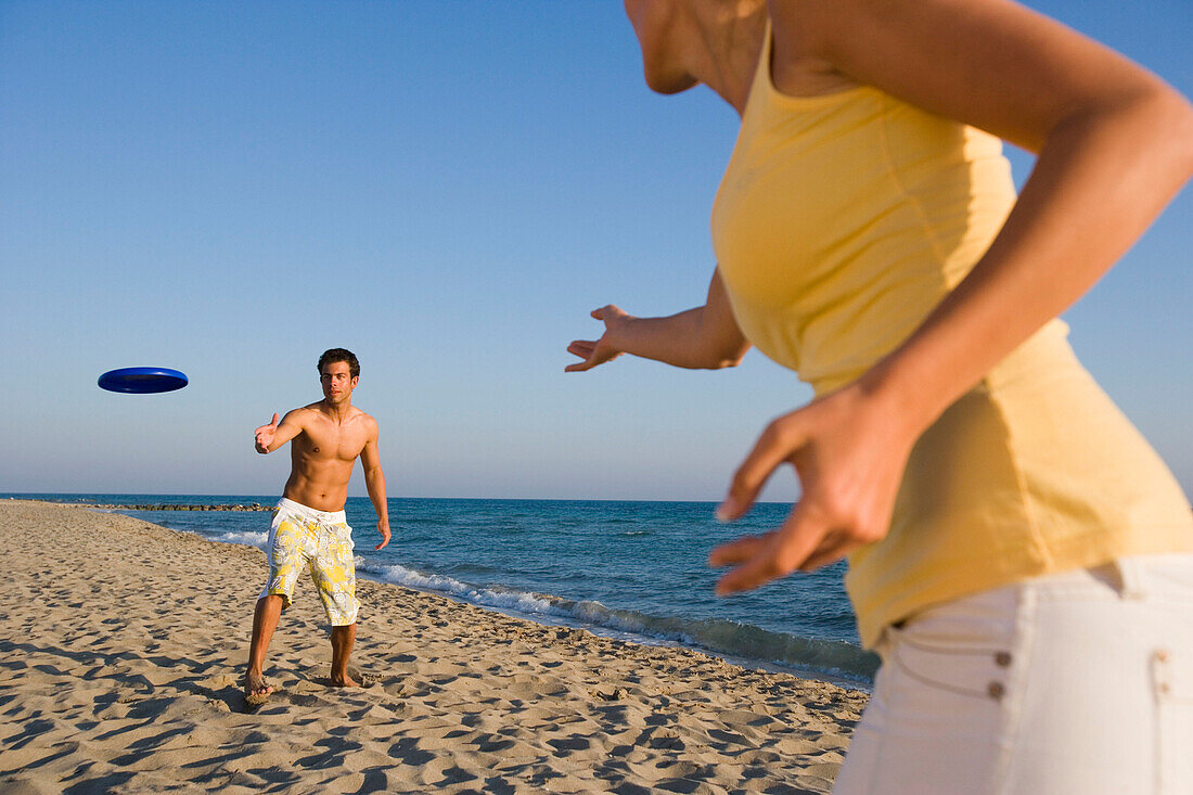 Young couple playing frisbee on beach, Apulia, Italy