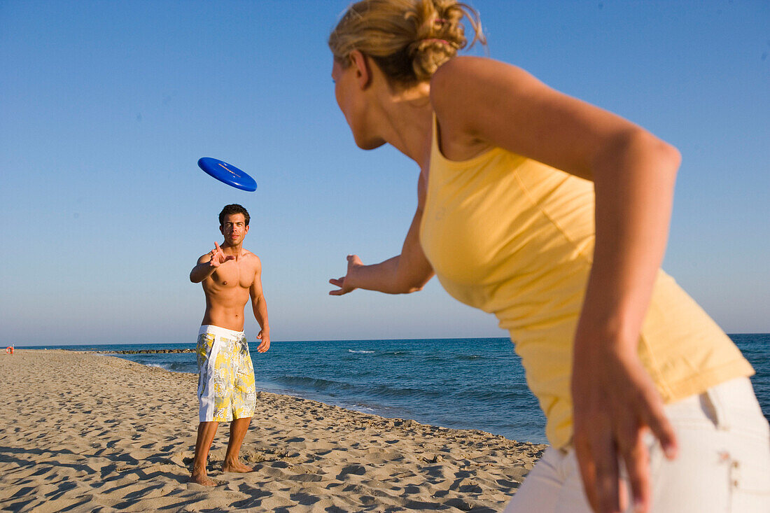 Young couple playing frisbee on beach, Apulia, Italy