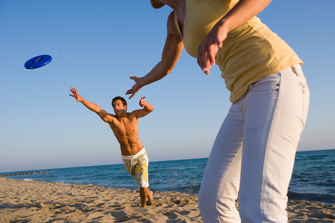 Young couple playing frisbee on beach, Apulia, Italy