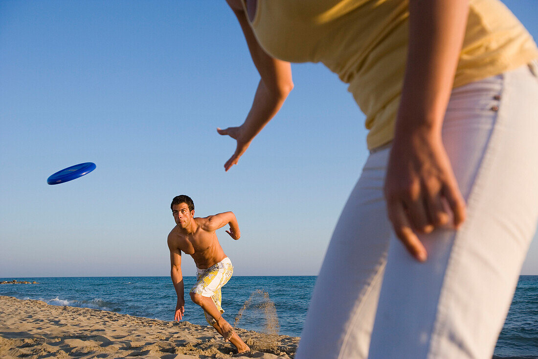 Junges Paar spielt Frisbee am Strand, Apulien, Italien