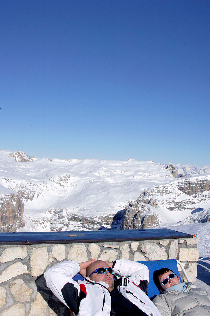 Touristen sonnen sich vor schneebedeckter Landschaft, Passo Pordoi, Dolomiten, Iitalien, Europa