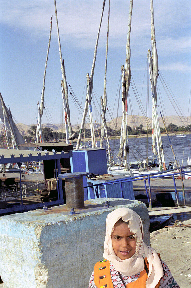 Ägyptisches Mädchen steht vor Segelbooten an einem Hafen am Nil, Luxor, Ägypten