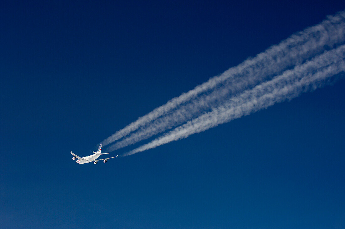 Flugzeug mit Kondensstreifen vor dunkelblauem Himmel