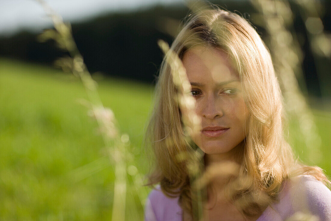 Young woman sitting on meadow, Blades of grass in foreground