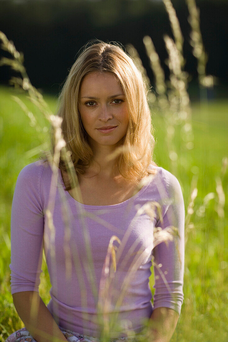 Young woman sitting on meadow, Blades of grass in foreground