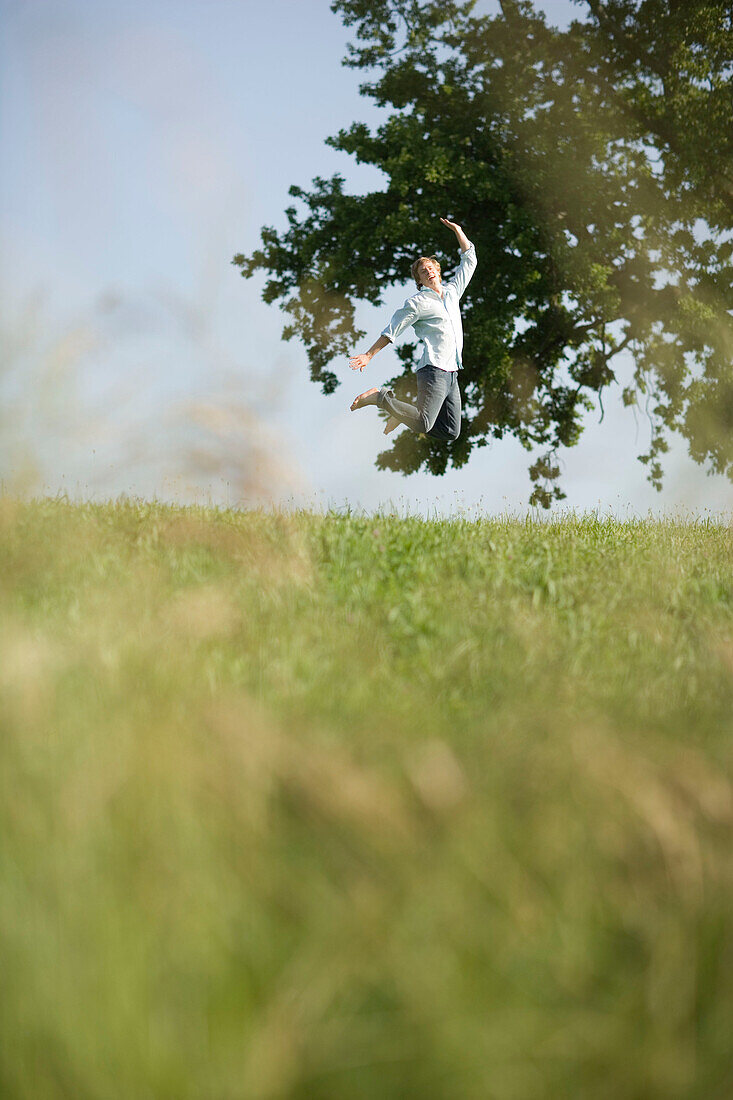 Junger springt in die Höhe auf einer Wiese