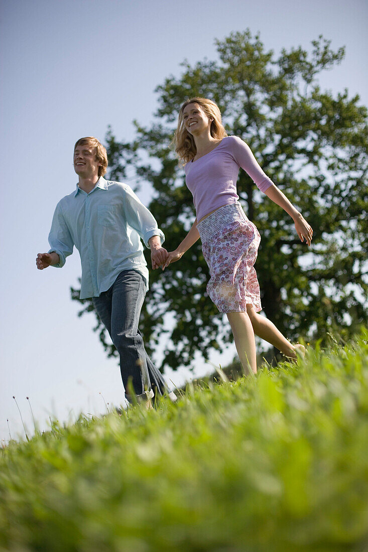 Couple running down on meadow holding hands