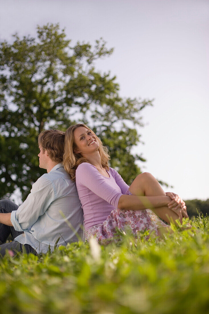 Couple sitting back to back on meadow