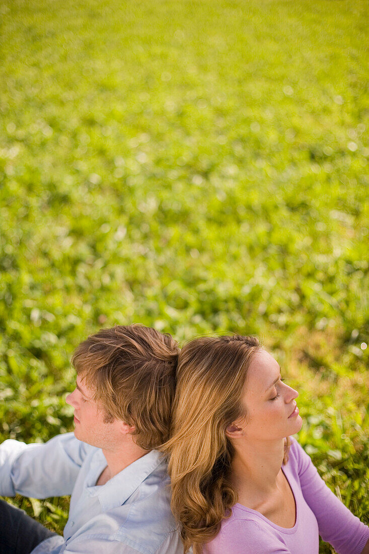 Junges Paar sitzen Rücken an Rücken in einer Wiese