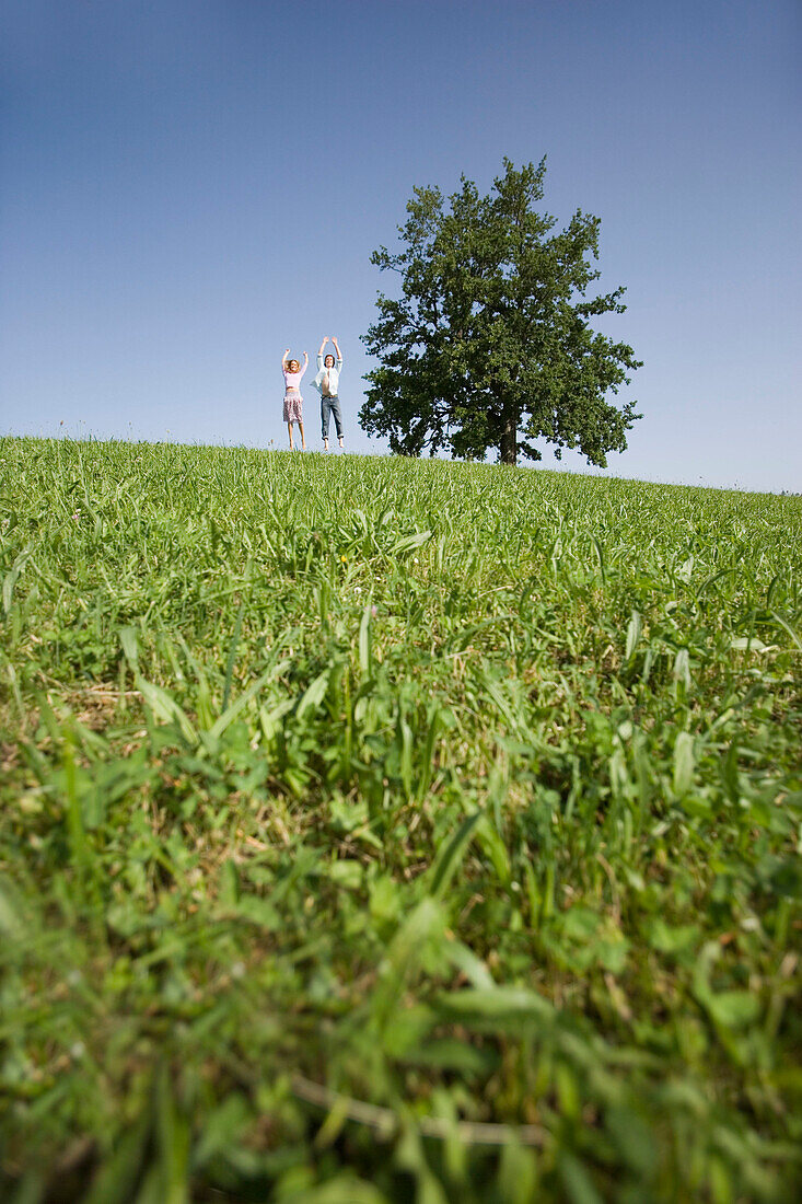 Couple jumping on meadow, raising arms