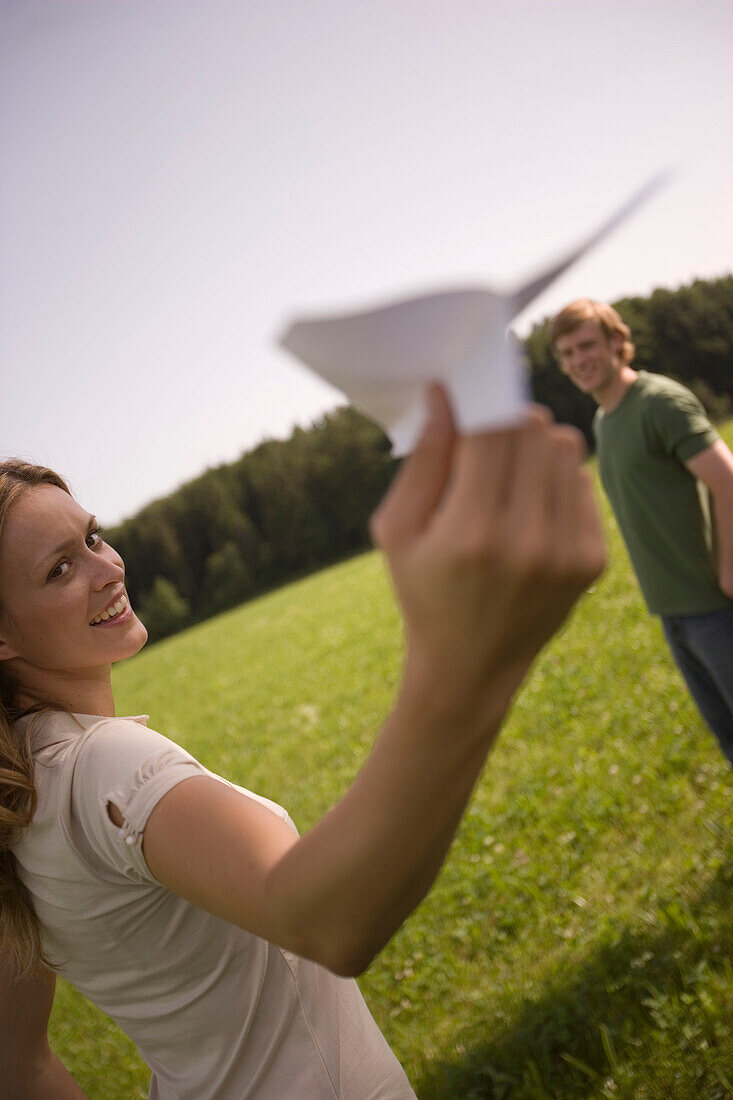 Junge Frau mit Papierflugzeug, auf einer Wiese