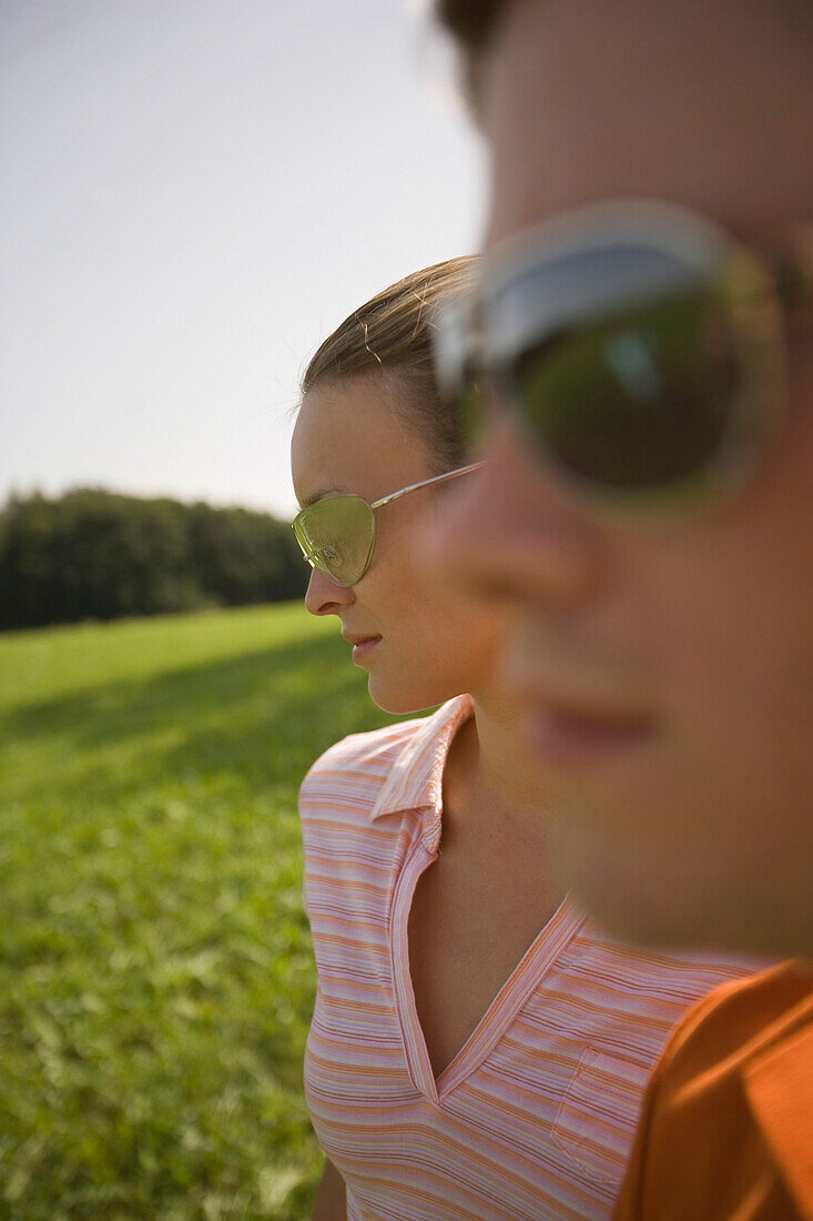 Two young people on meadow, both wearing sunglasses, close-up