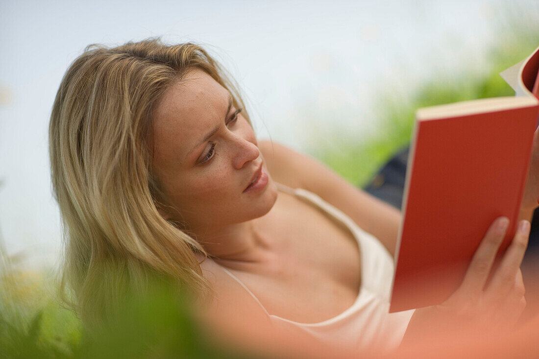 Junge Frau liegt in der Wiese und liest ein Buch