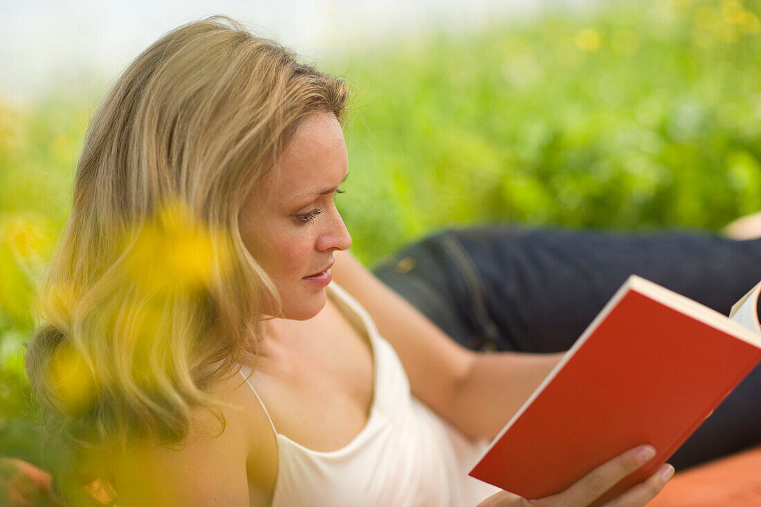 Junge Frau liegt in der Wiese und liest ein Buch