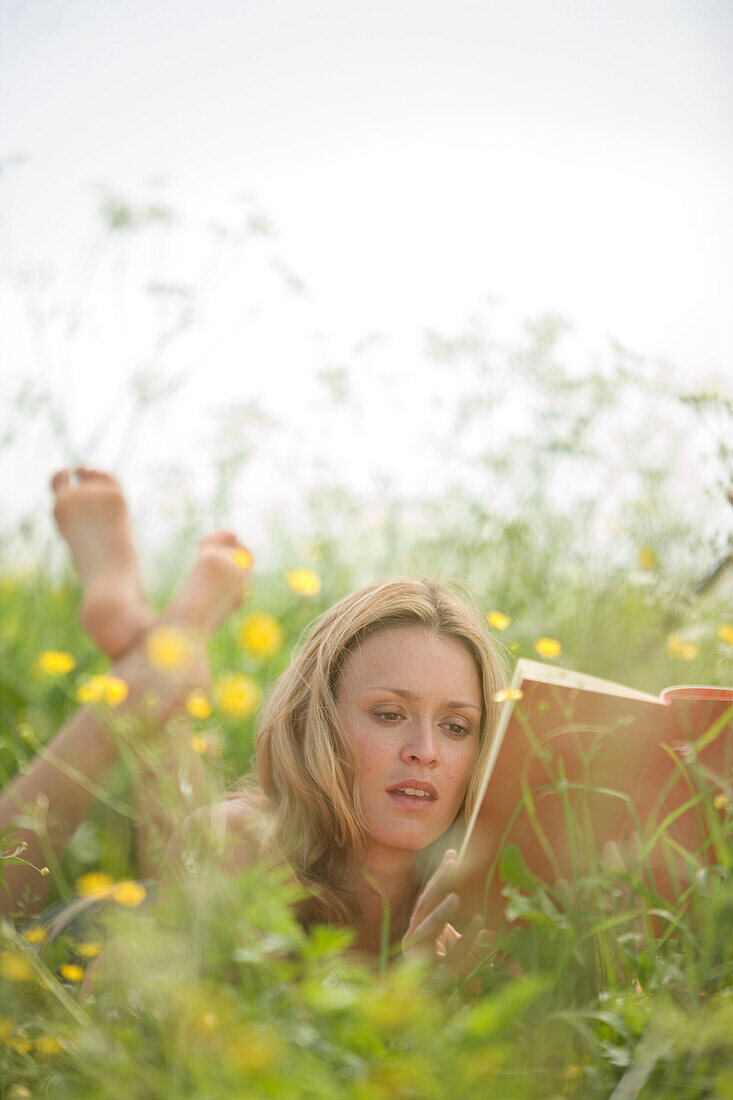 Young woman lying on meadow and reading book