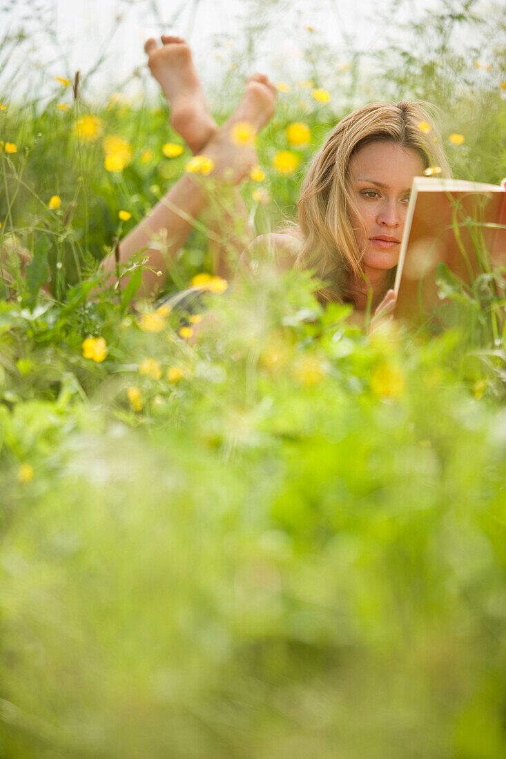 Junge Frau liegt in der Wiese und liest ein Buch