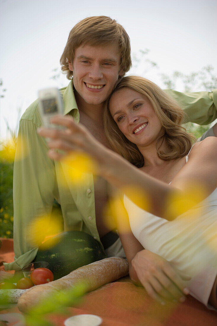 Young couple on meadow, woman taking picture with camera phone
