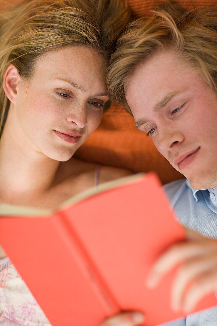 Young couple lying on blanket and reading together a book