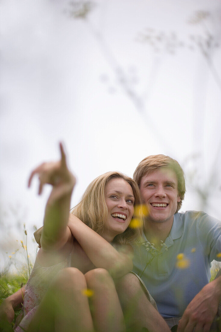 Young couple sitting on meadow, woman pointing