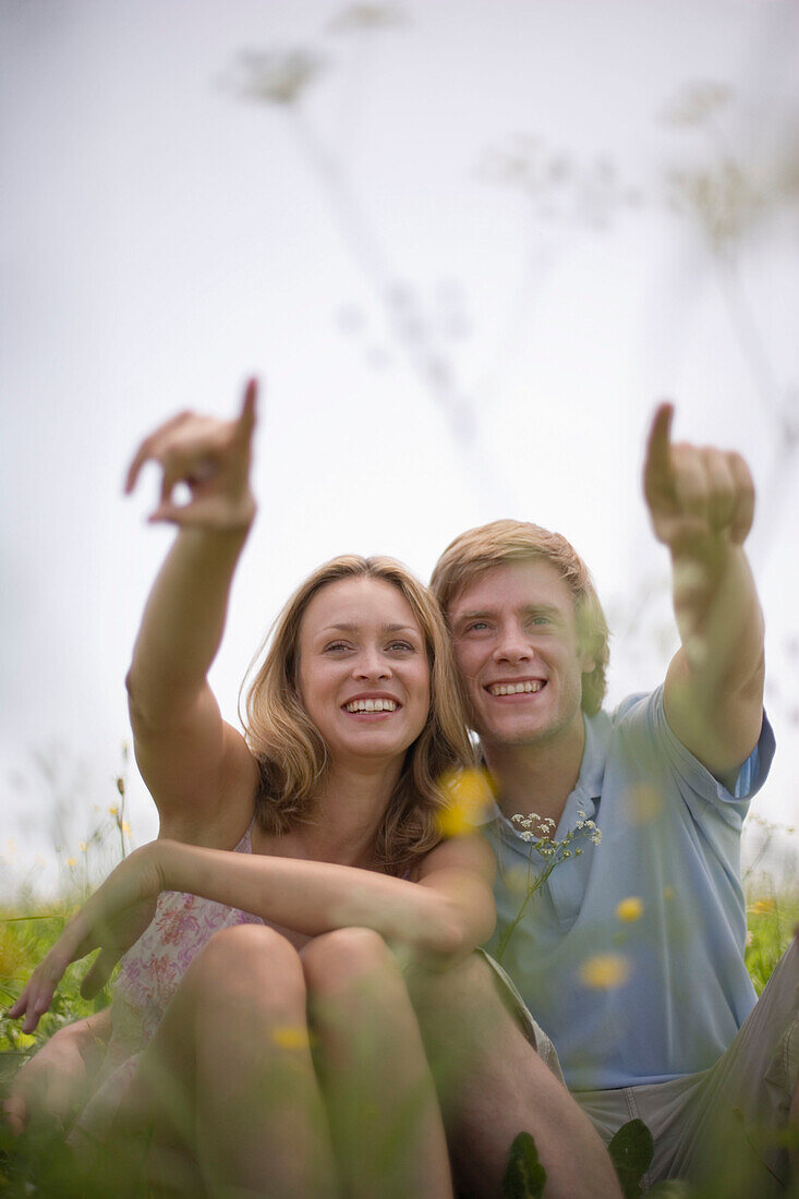 Young couple sitting on meadow, both pointing