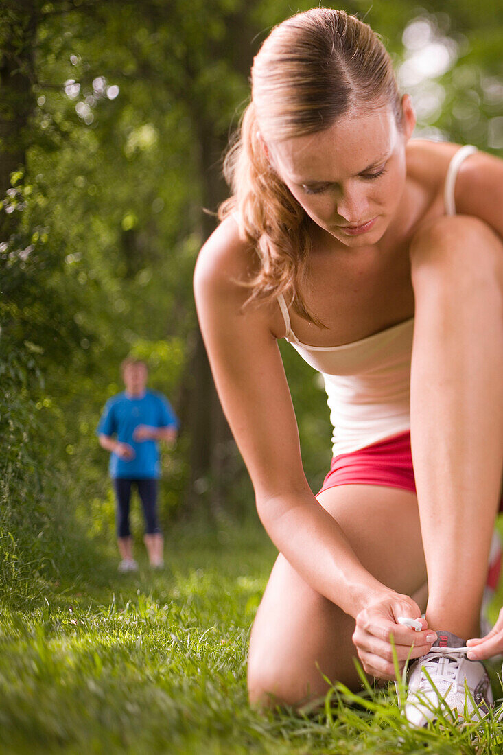 Junge Joggerin bindet Ihre Schnürsenkel, junger Mann im Hintergrund